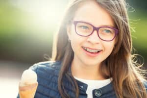 Teen girl with glasses smiling while eating ice cream, demonstrating living with braces as a teenager